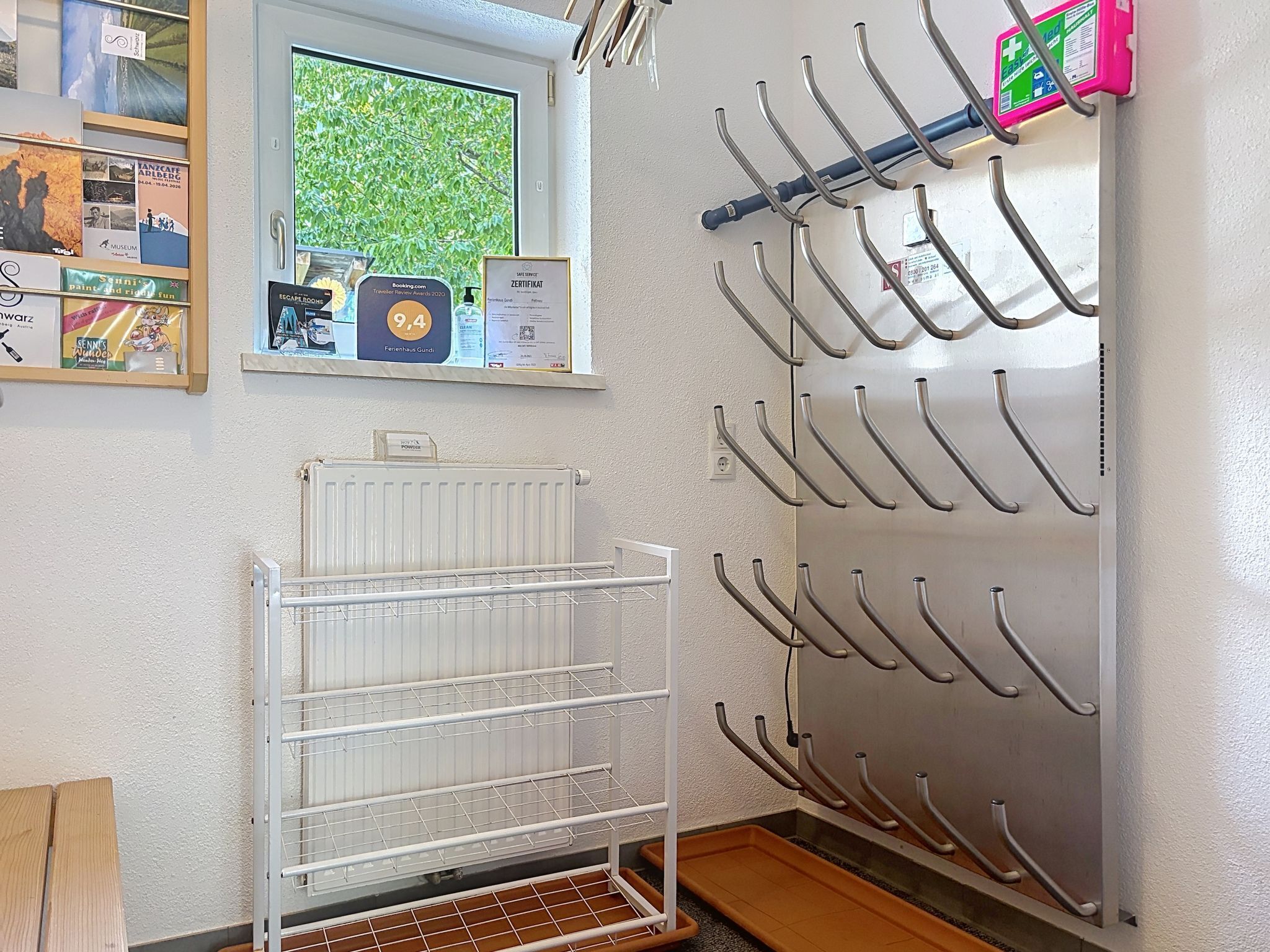 A room with a window, a radiator, a wall-mounted rack with hooks, and a shelf with various items.