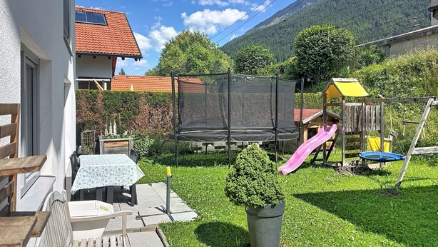 Un giardino sul retro con un trampolino, uno scivolo, una casetta da gioco e un tavolo con sedie.
