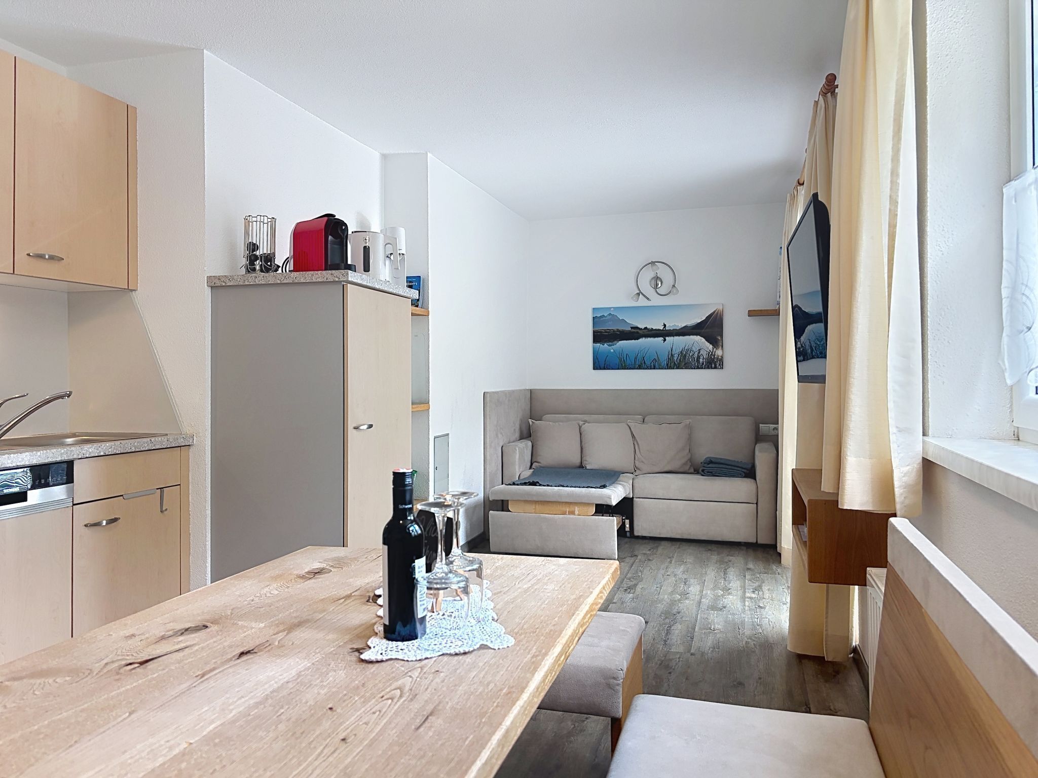 Een ruimtelijke woonruimte met een kitchenette, een eethoek en een zithoek met een bank en een tafel.