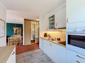 Eine moderne Küche mit weißen Schränken, einem eingebauten Backofen und einem Essbereich mit Holztischen und -stühlen.