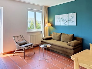 Ein Zimmer mit Sofa, Sessel, kleinem Tisch und einem Kunstwerk an der Wand.