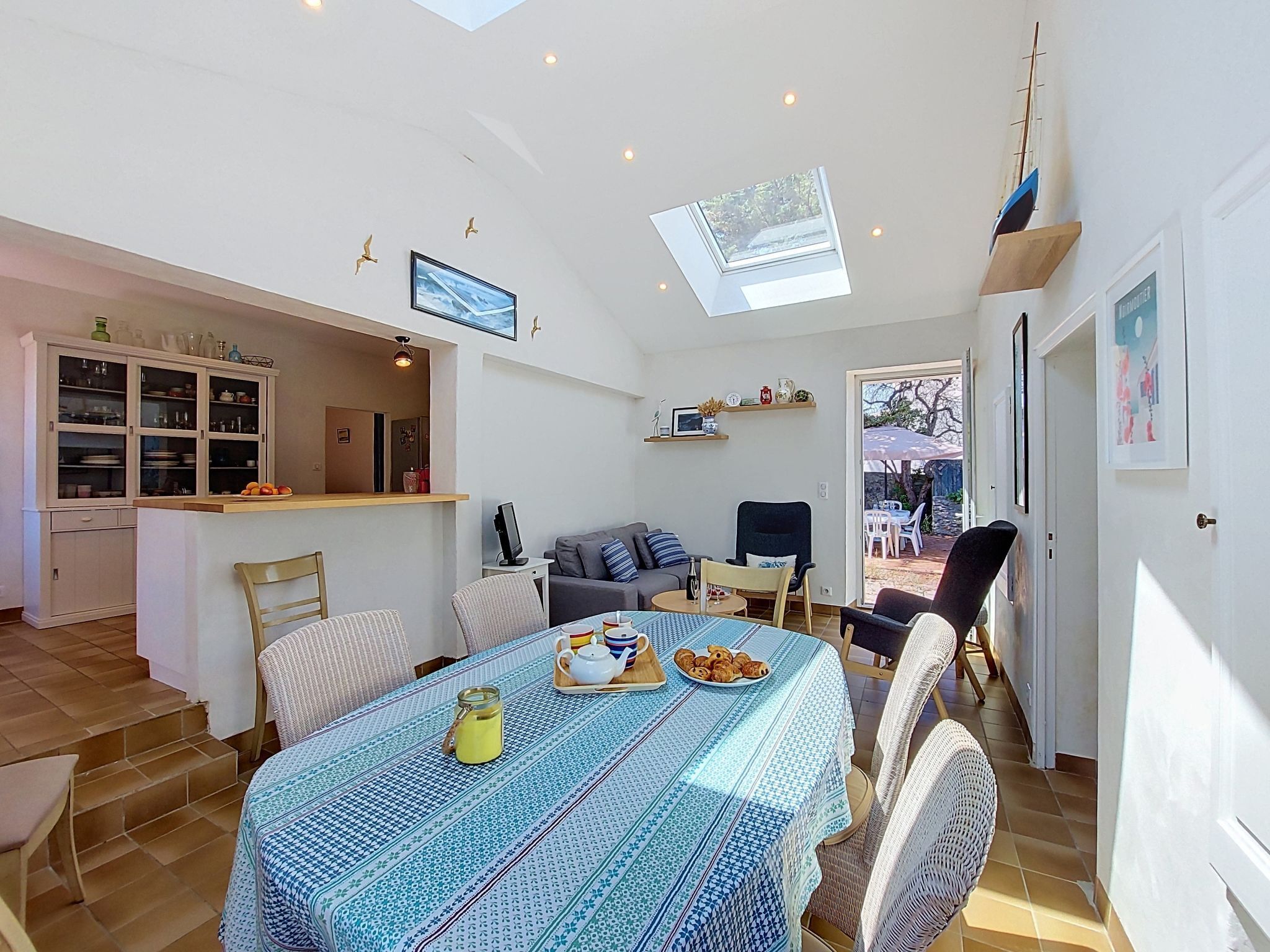Amplia sala de estar con mesa y sillas de comedor, sofá y televisor. Cuenta con una zona de cocina con armarios y ventana.