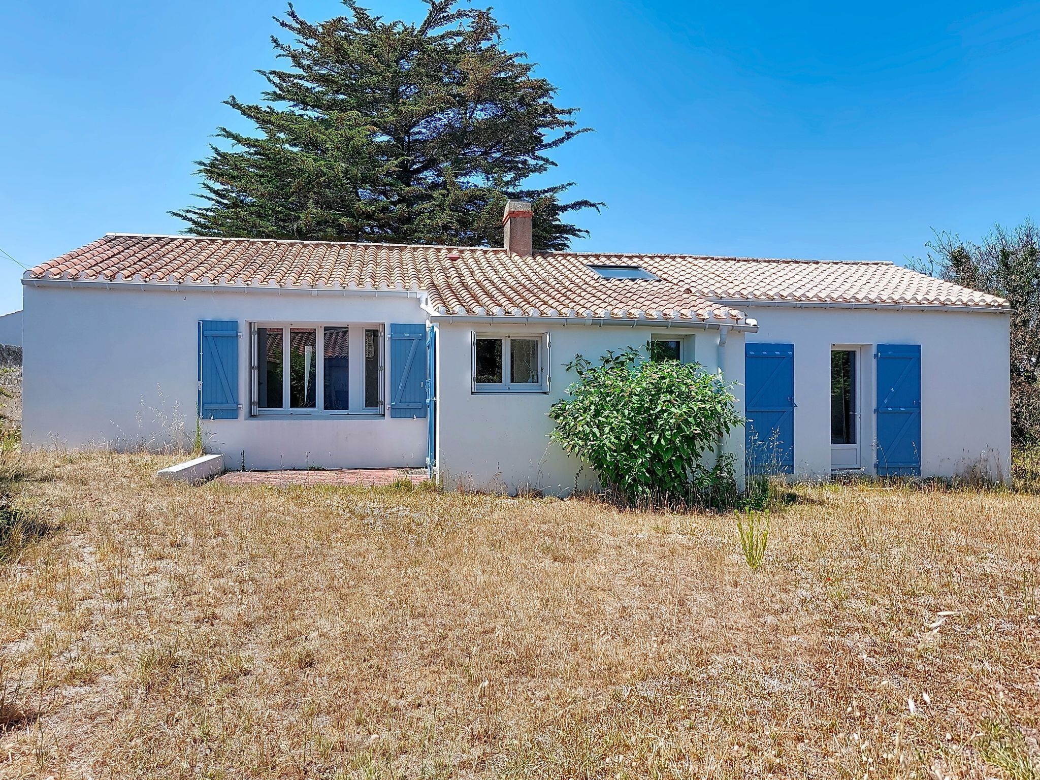 Un bâtiment d’un seul étage, avec un toit recouvert de tuiles, un petit porche et un arbuste devant.