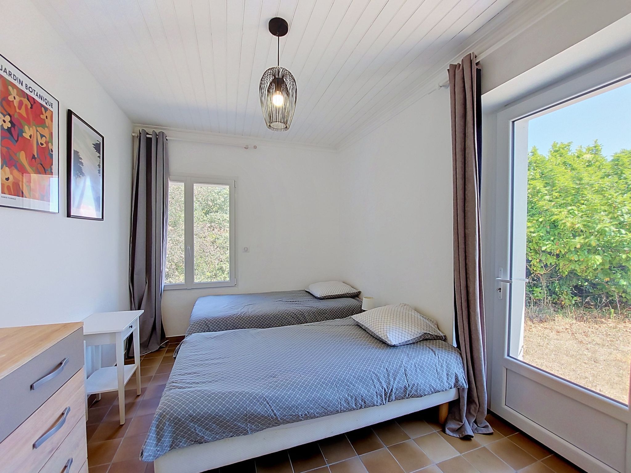 Un dormitorio con dos camas, una ventana con cortinas, un aparador de madera y una lámpara colgante.