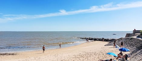 Ein sandiger Strand mit einem steinernen Wellenbrecher, blauem Himmel und ruhiger See.