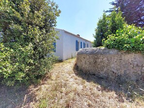A narrow path leading to a building with blue shutters, surrounded by dense foliage. - Villa La Coquille by Interhome (Ile de Noirmoutier)