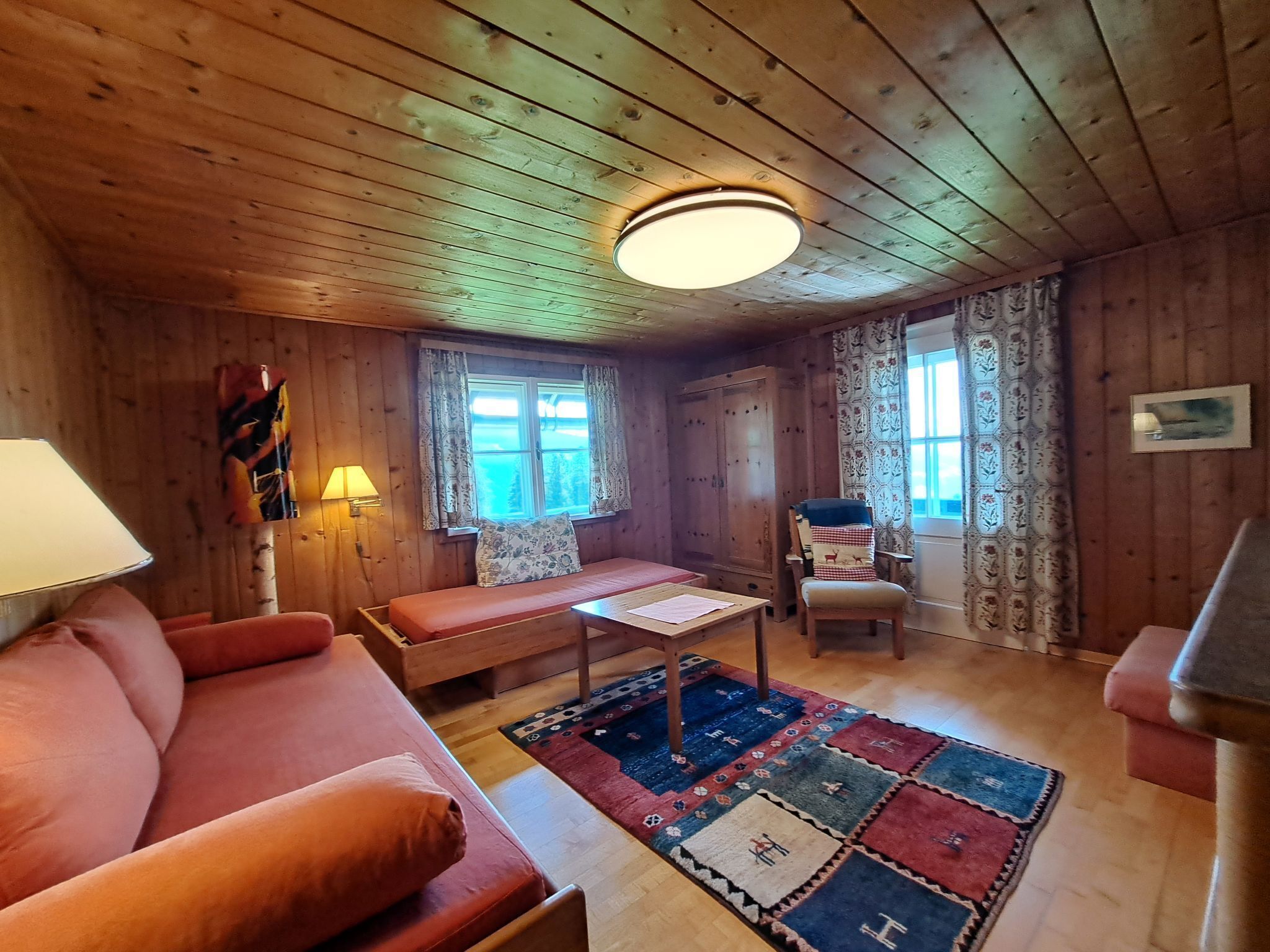 Ein gemütliches Blockhaus-Interieur mit Holzbalkendecke, einer Couch, einem Tisch und einem gemusterten Teppich.