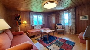 Interior acolhedor de uma cabana com teto de madeira, um sofá, uma mesa e um tapete estampado.