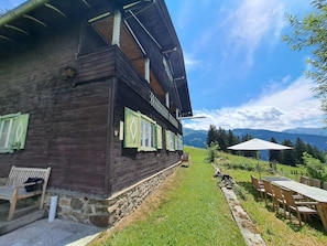 A wooden building with a stone foundation, a bench, and outdoor seating with umbrellas.