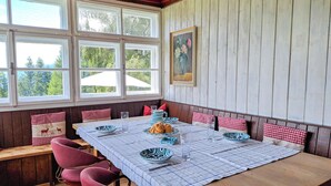 Uma sala de jantar com uma mesa comprida, cadeiras estofadas vermelhas e toalha de mesa xadrez.