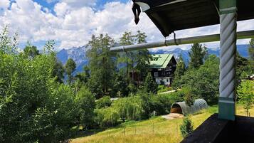 Eine Berghütte mit grüner Dachdeckung, umgeben von dichtem Wald und Bergen im Hintergrund.