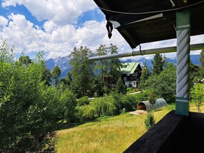 Eine Berghütte mit grüner Dachdeckung, umgeben von dichtem Wald und Bergen im Hintergrund.