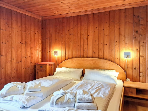 A wooden-paneled room with a bed, two bedside tables, and wall-mounted lights.