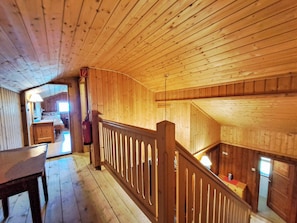 A wooden interior with a staircase, a fire extinguisher, and a view of a room with a bed.