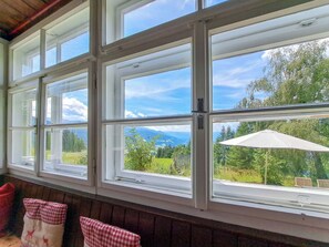 Quarto com grandes janelas que oferecem vista para uma paisagem verde e montanhas.
