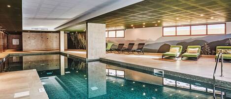 Una piscina interior con suelo de baldosas, sillones de descanso y un mural en la pared.