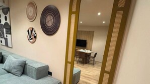 Una sala de estar moderna con un sofá gris, un comedor con mesa y sillas, y un espejo grande con un marco decorativo.