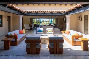 Ein großzügiger Außenbereich mit mehreren Sofas und Holztischen, eine Terrasse mit Fliesenboden und Blick auf den Außenessbereich.