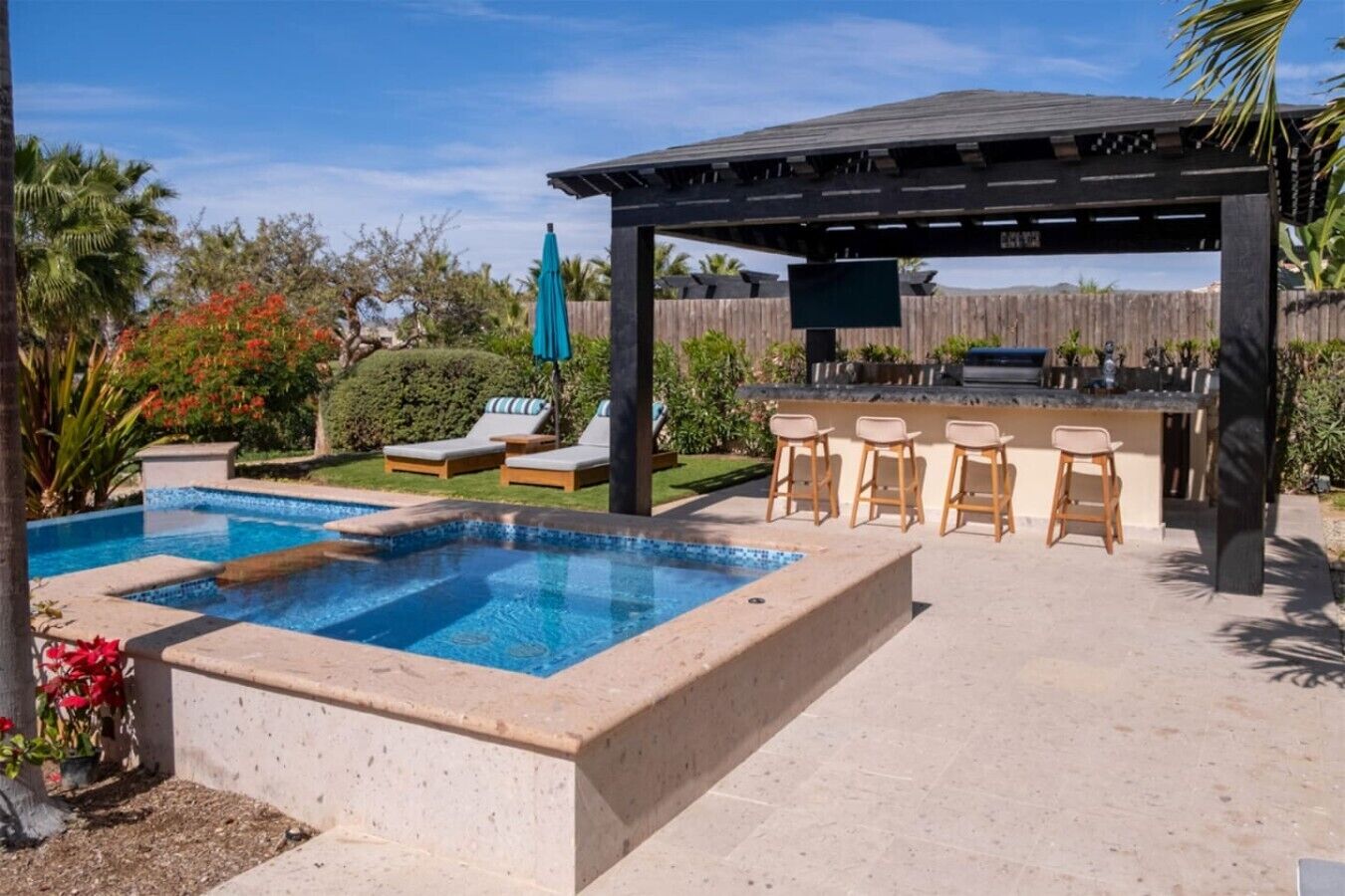 Un patio trasero con piscina, sillas de descanso, zona de barbacoa y una pérgola.