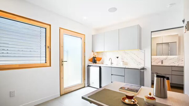 A modern kitchen with a dining area, a window with blinds, and a countertop with a kettle. - Award-Winning Eco Retreat with Fresh Air - certified Passive House (Los Angeles)