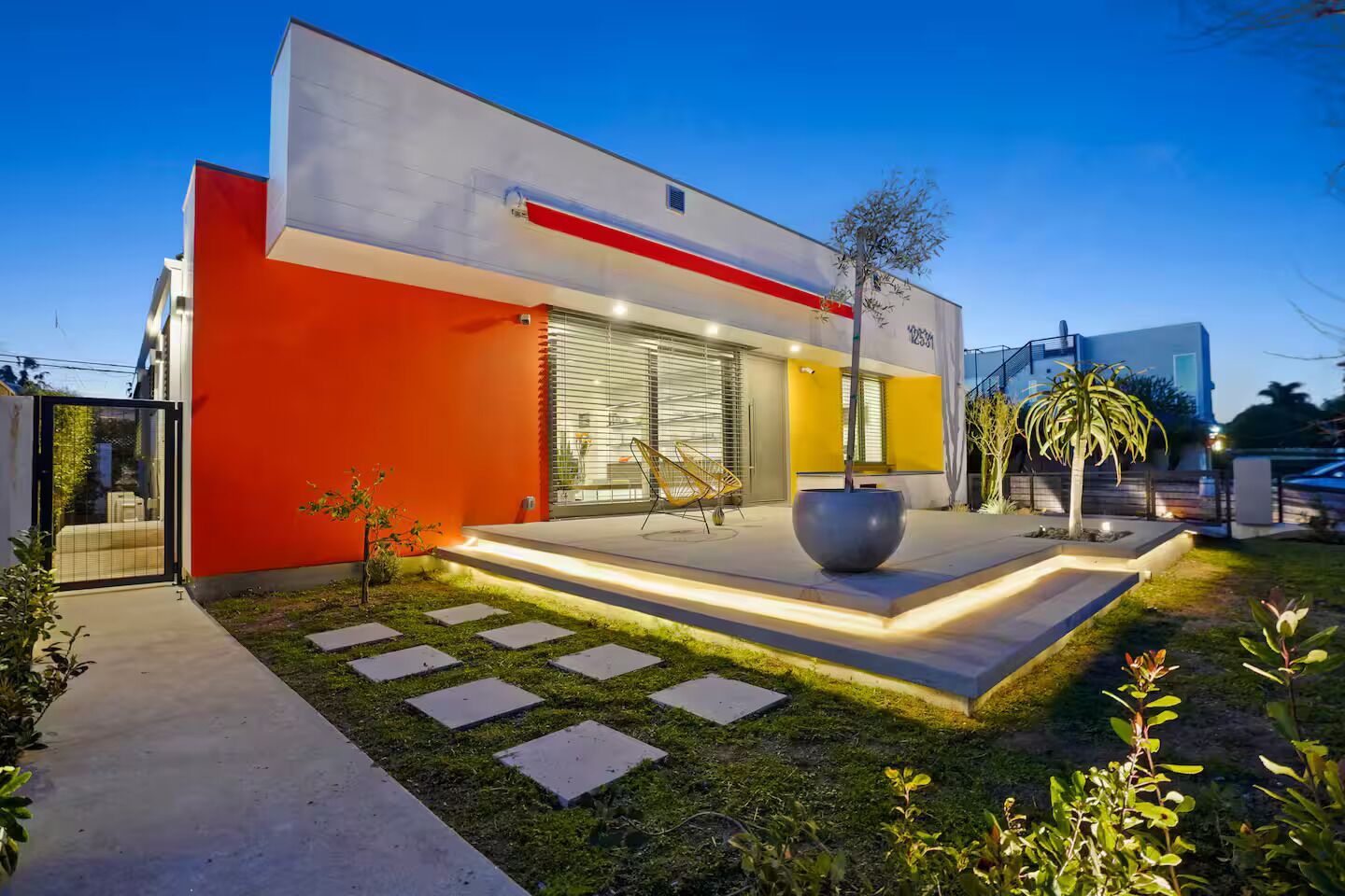 A modern house with a red and yellow facade, a large outdoor seating area, and a well-maintained garden.