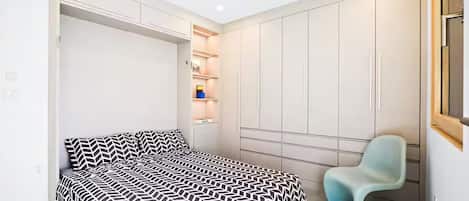Un dormitorio con cama, una silla y armarios empotrados.