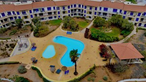 Oversigtsbillede af et hotel med swimmingpool, flere balkoner og anlagte haver.
