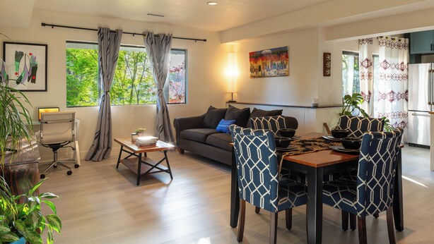 A modern living room with a sofa, dining table, chairs, and a kitchen in the background.