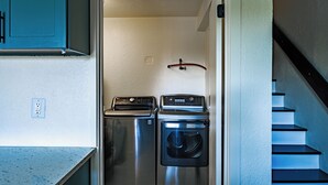 A compact laundry area with two washing machines and a dryer, a staircase to the right, and a power outlet on the left wall.