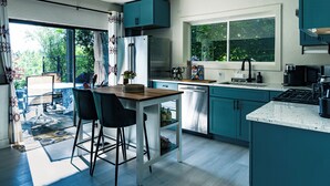 A modern kitchen with teal cabinets, a stainless steel refrigerator, and a large window overlooking greenery.