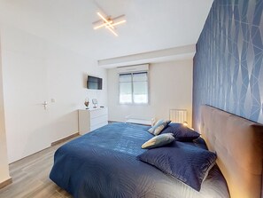 Ein Schlafzimmer mit einem Bett, einem Fernseher, einem Fenster mit Jalousien und einer Wand mit Muster.
