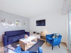 Ein modernes Wohnzimmer mit einer Couch, einem Couchtisch, einem Fernseher und einem Sessel.