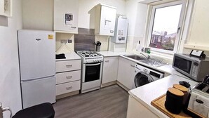 Een kleine keuken met een koelkast, fornuis, magnetron, spoelbak en wasmachine.