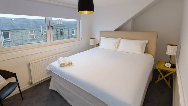 Hotelkamer met een groot bed, een raam met uitzicht op gebouwen, een nachtkastje met een lamp en een stoel.