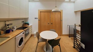 Een kleine keuken met een wasmachine, een eettafel en een plafondlamp.