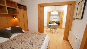 Een slaapkamer met een bed, een houten kast, een klein tafeltje met stoelen, en een radiator.