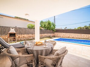 Eine Terrasse mit Pool, Korbmöbeln und einem Grill.
