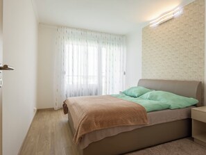 A bedroom with a bed, a bedside table, a window with sheer curtains, and a geometric-patterned wall. - Apartment Silver by Interhome (Siofok)