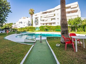 A swimming pool with a green deck, red chairs, and a palm tree. - Las Naciones by Interhome (Benalmádena Costa)