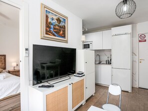 Quarto de hotel moderno com uma grande TV de tela plana, um quadro, uma kitchenette e uma cama.