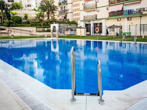A swimming pool with metal ladders, a stone archway, and a building with balconies in the background. - Las Naciones by Interhome (Benalmádena Costa)