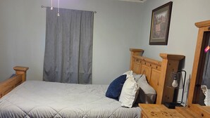A bedroom with a bed, wooden dresser, ceiling fan, and a framed picture on the wall.