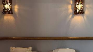 Habitación de hotel con cama, dos lámparas de pared, una cesta de mimbre con toallas y un equipo de aire acondicionado.