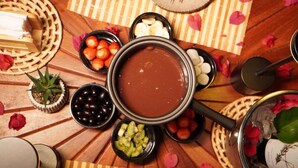 Una mesa de comedor con una fuente de fondue de chocolate en el centro, rodeada de tazones con frutas y nueces.