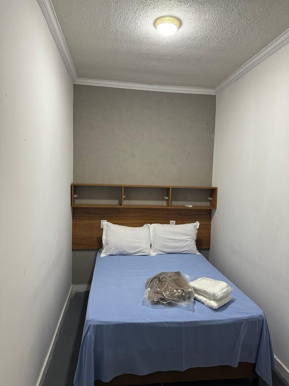 Una habitación pequeña con una cama individual, cabecera de madera y una lámpara en el techo.