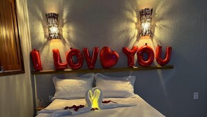 A bed with a white bedspread, a heart-shaped decoration, and red balloons spelling 'I LOVE YOU' on the wall.