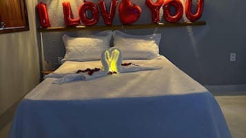 En seng med et hvidt lagen, en hjerteformet dekoration og røde balloner der staver 'I LOVE YOU' på væggen.