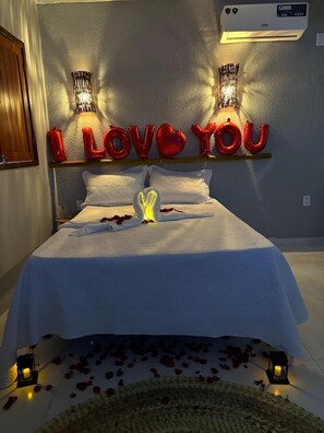 A bed with a white bedspread, a heart-shaped decoration, and red balloons spelling 'I LOVE YOU' on the wall.