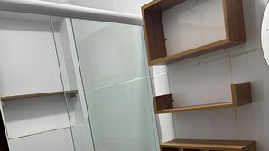 A bathroom with a glass shower enclosure, a toilet, and wooden shelves above the sink.