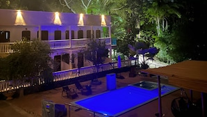 Un edificio con zona de piscina, mobiliario exterior e iluminación destacada en la fachada.